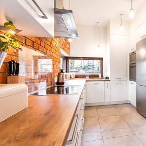 Kitchen with white units, wooden wheat, marble floor and red brick wall